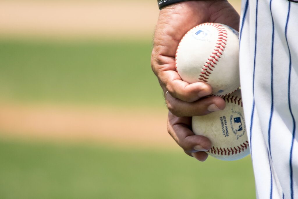 A close-up of a person in a pinstripe uniform holding two baseballs in their hand, standing on a grassy baseball field.