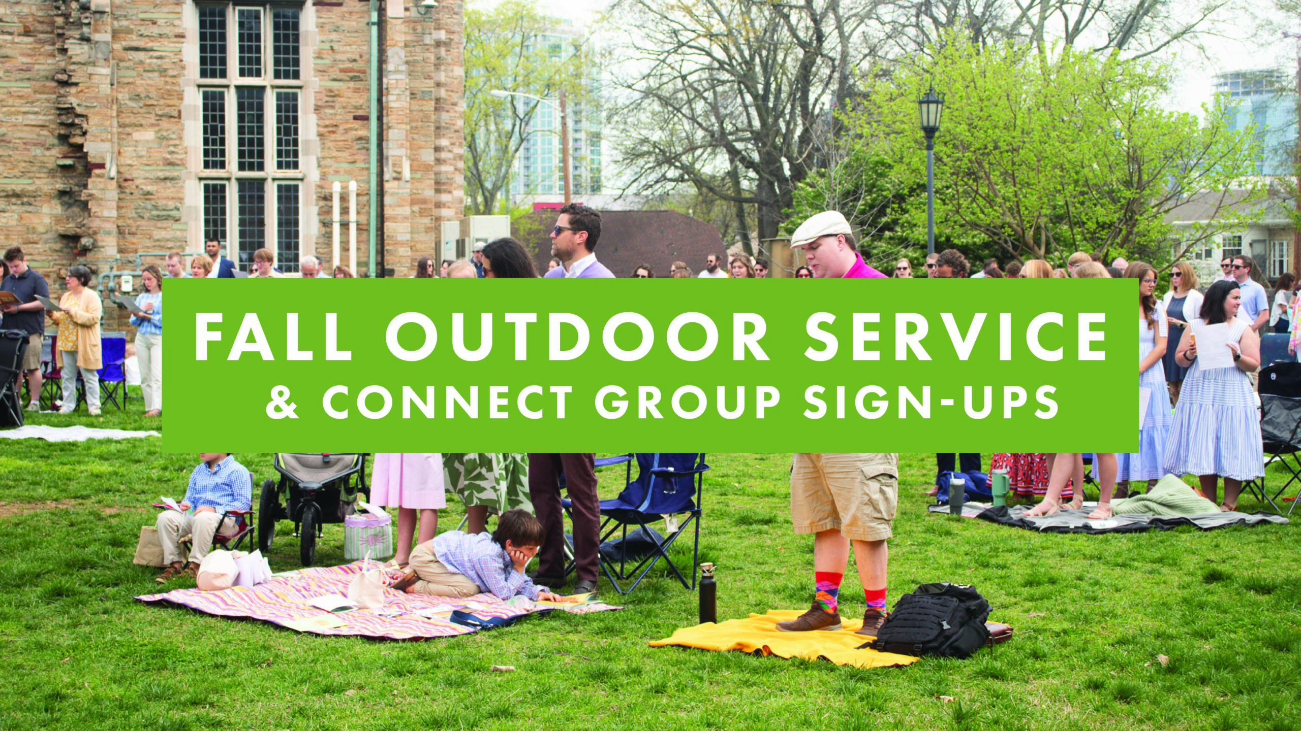 People gather on a lawn outside a stone building for an event. Some sit on blankets and lawn chairs. Large green banner reads: FALL OUTDOOR SERVICE & CONNECT GROUP SIGN-UPS.